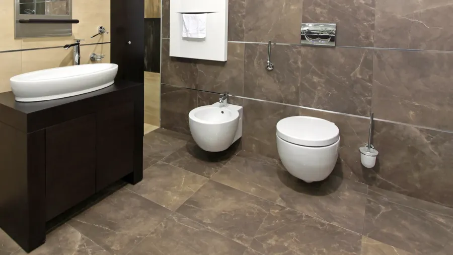 A bathroom interior with vessel sink, wall mounted toilet, and large format tiles.