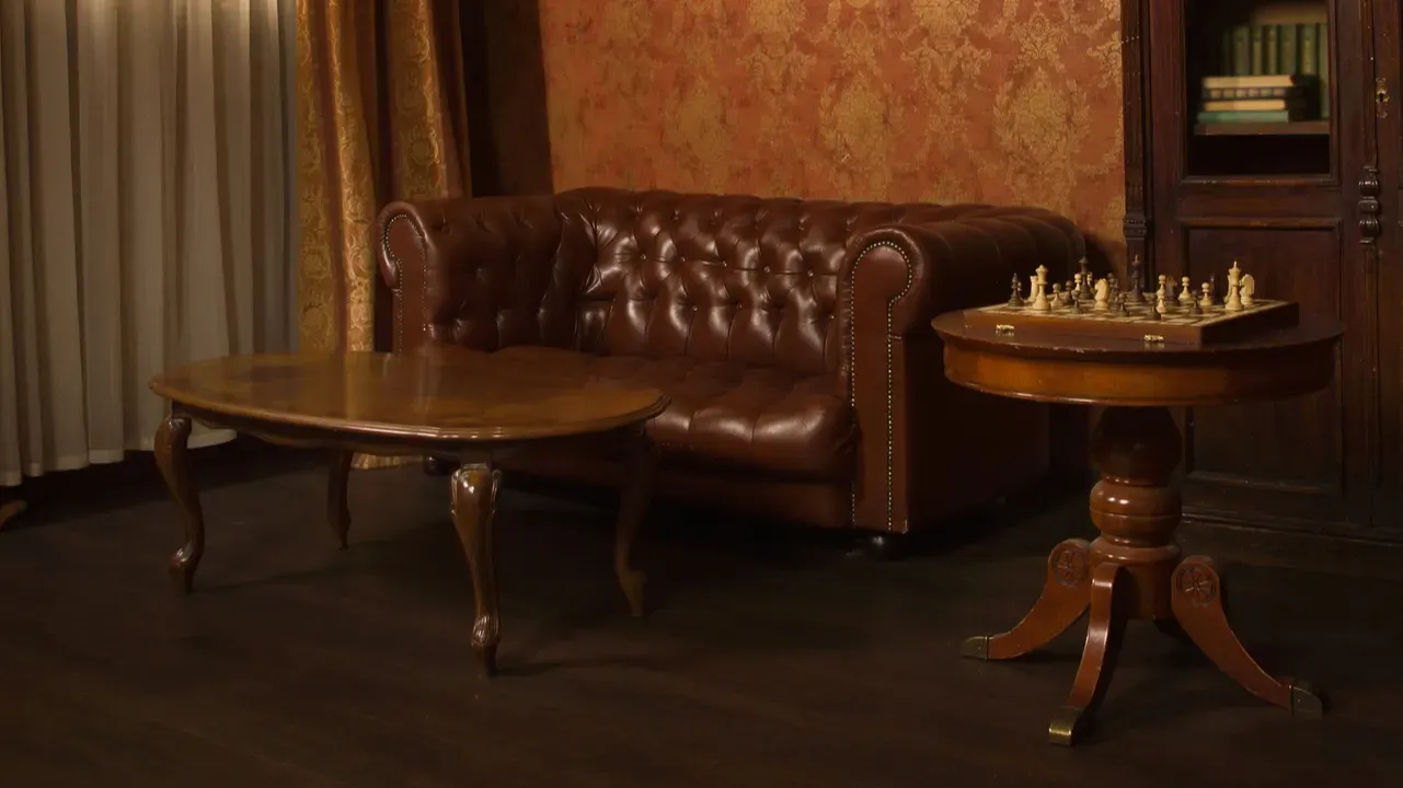Antique and vintage coffee table and sofa in a room with sheer curtains, book shelf, and vintage wallpaper.