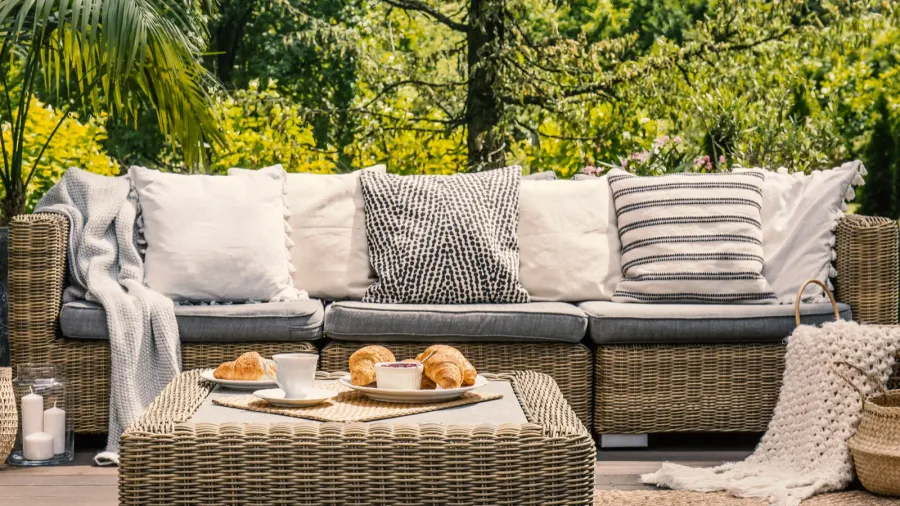 Cozy outdoor patio with a wicker sofa, cushions, and a table set for breakfast.