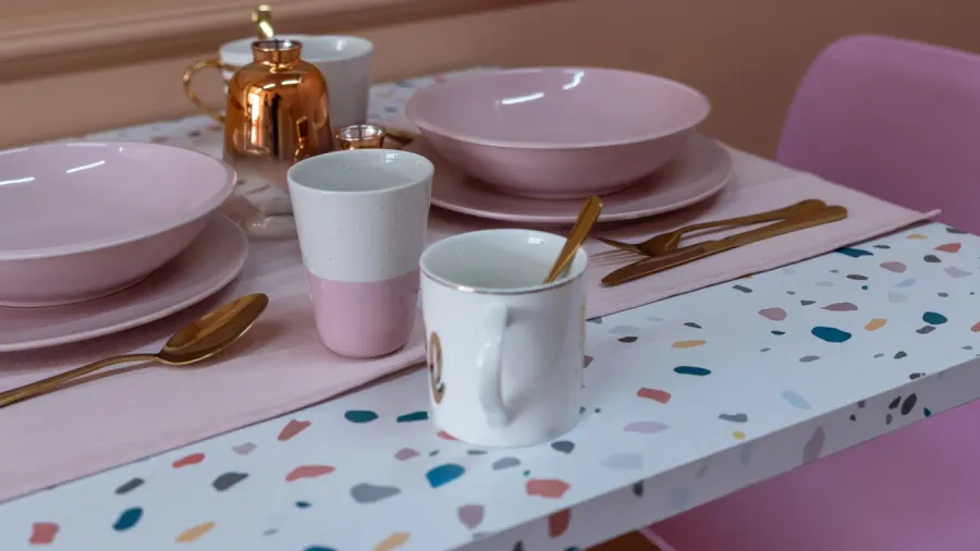 A terrazzo table with pink and white dinnerware and copper utensils.