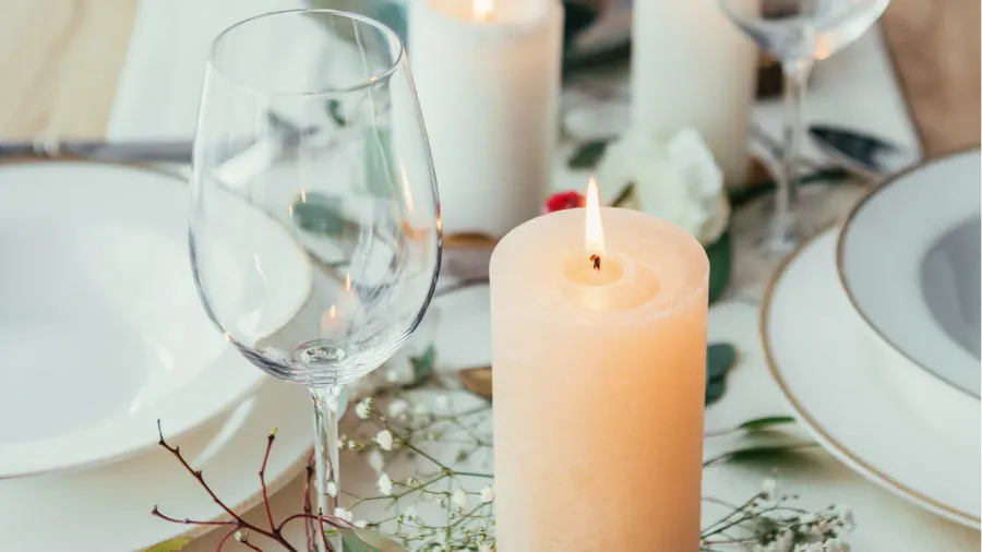 Close-up of a burning candle and a glass on a beautiful table setting with baby's breath flowers and dinnerware.