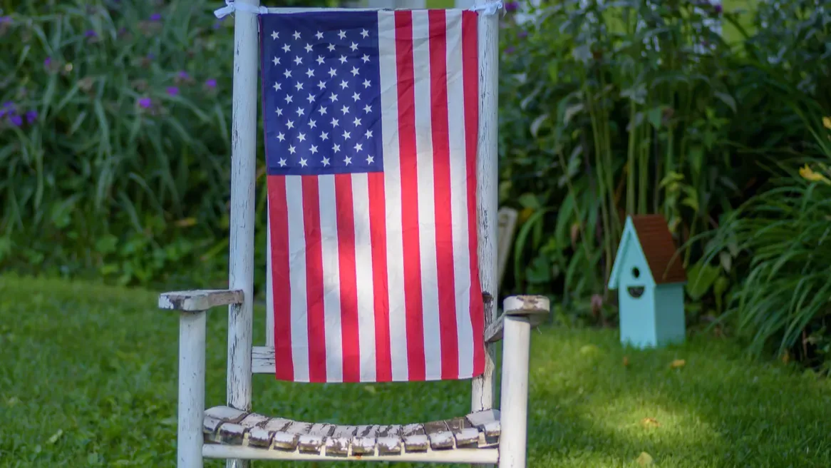 An empty rustic rocking chair with the American flag on it.