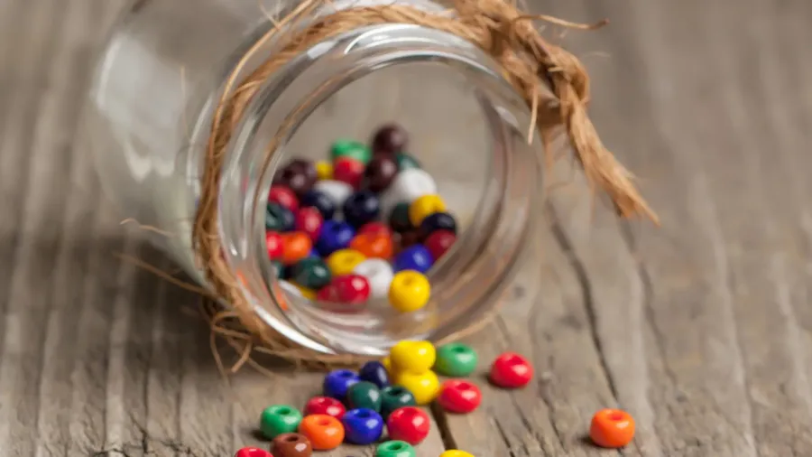 Colorful beads in a glass jar on a wooden table.