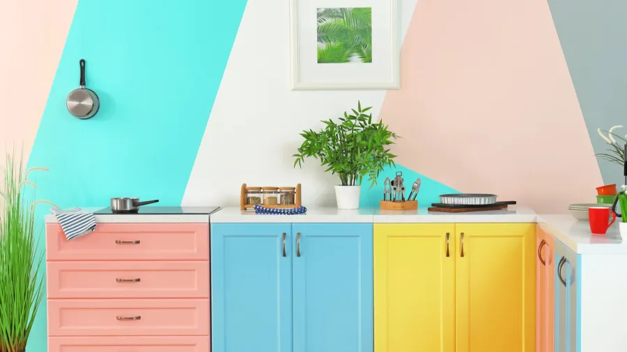 Bright, pastel-colored kitchen with geometric wall design, blue and yellow cabinets, and potted plants.