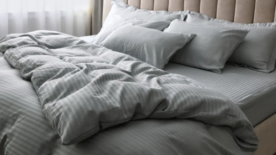 A comfortable bed with gray bedding, pillows, and blanket.