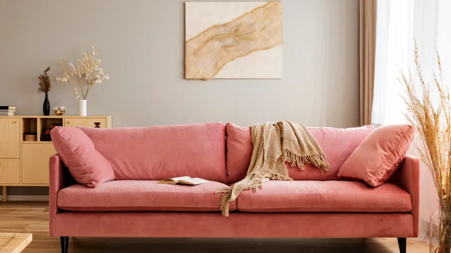 A pastel pink couch with pillows and throw blanket in a beige living room.