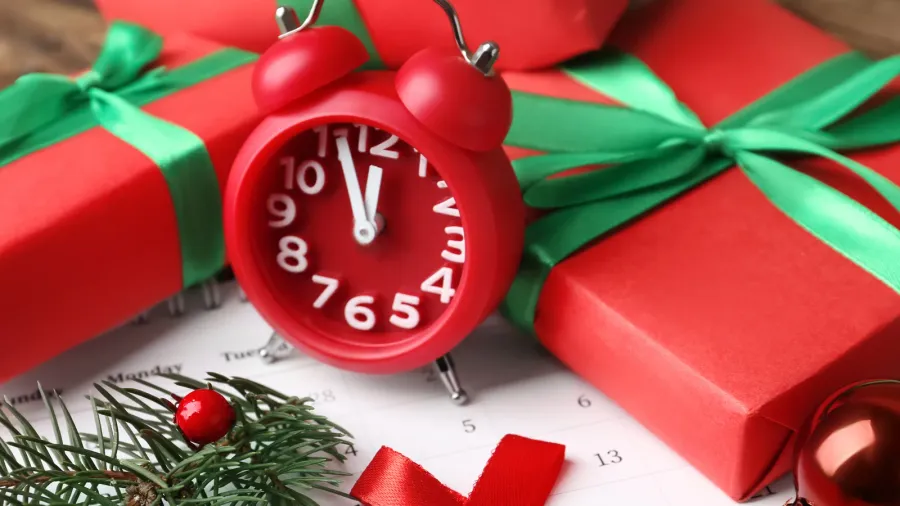 A red alarm clock next to wrapped gifts with green ribbons and pine branches.