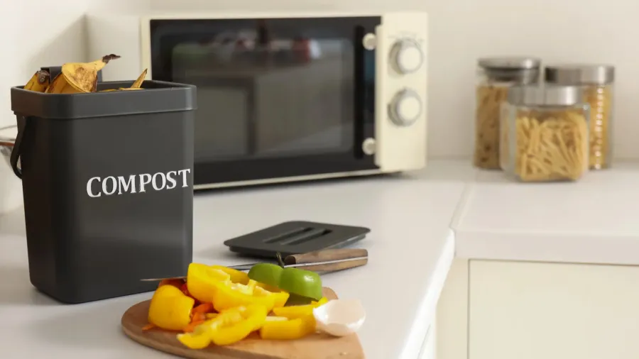 container for compost and cutting board with food on counter