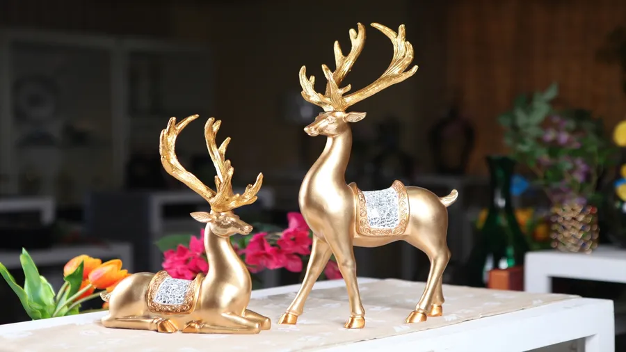 Two golden deer figurines placed on a white table with a runner.