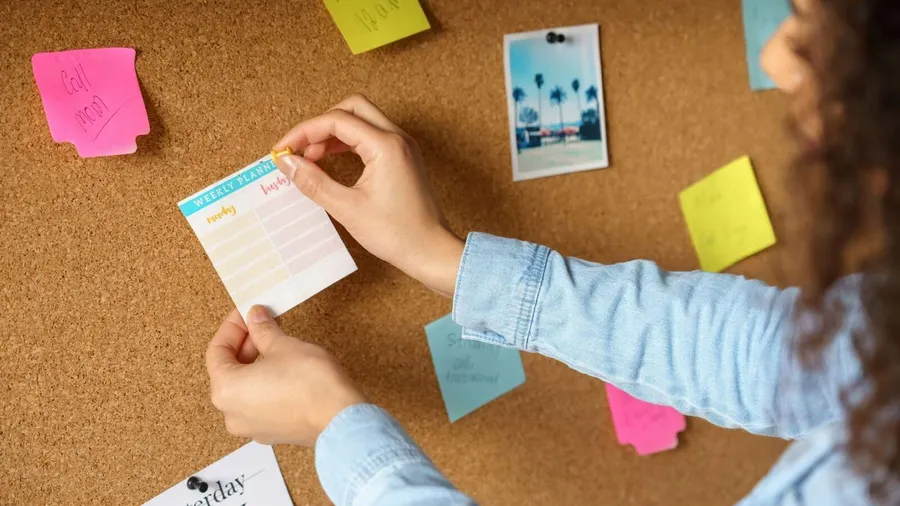 A woman attaching weekly planner on a cork bulletin board.