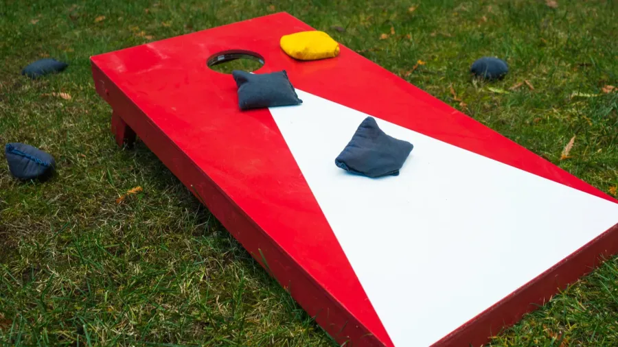 Close-up of a cornhole game with a red and white board on grass, with bean bags.