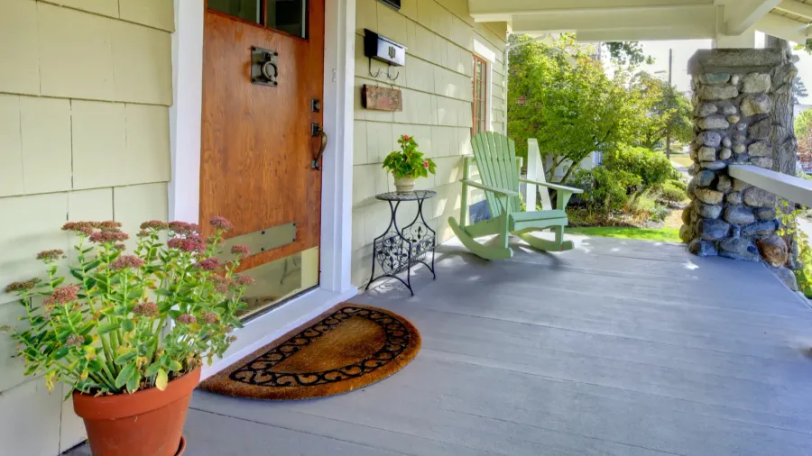 A front porch featuring a door, potted plants, and a decorative welcome mat.