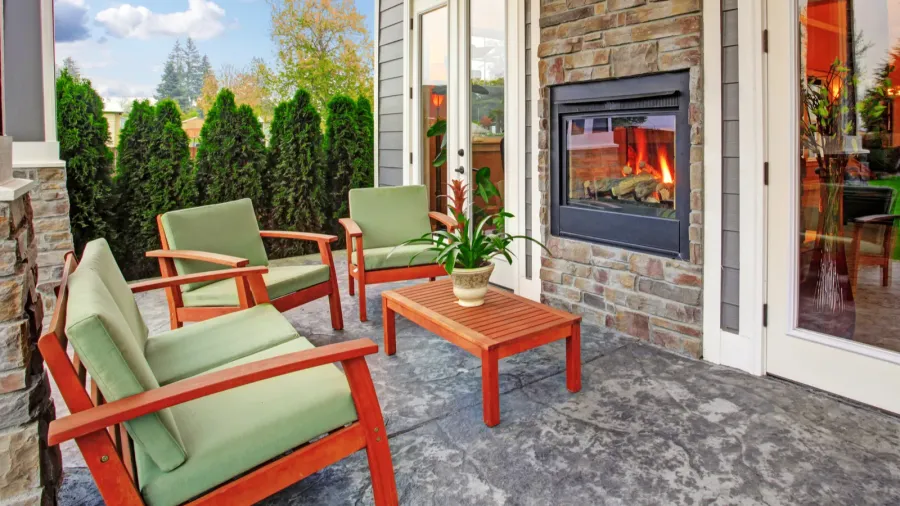 An outdoor seating area with green chairs, a wooden table, and a fireplace.