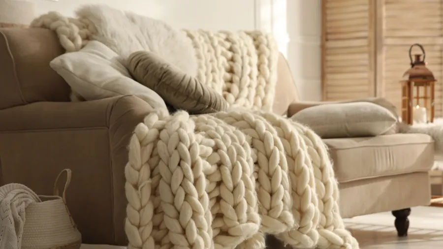 A cozy living room interior with a chunky knit throw blanket and throw pillows on a beige sofa.