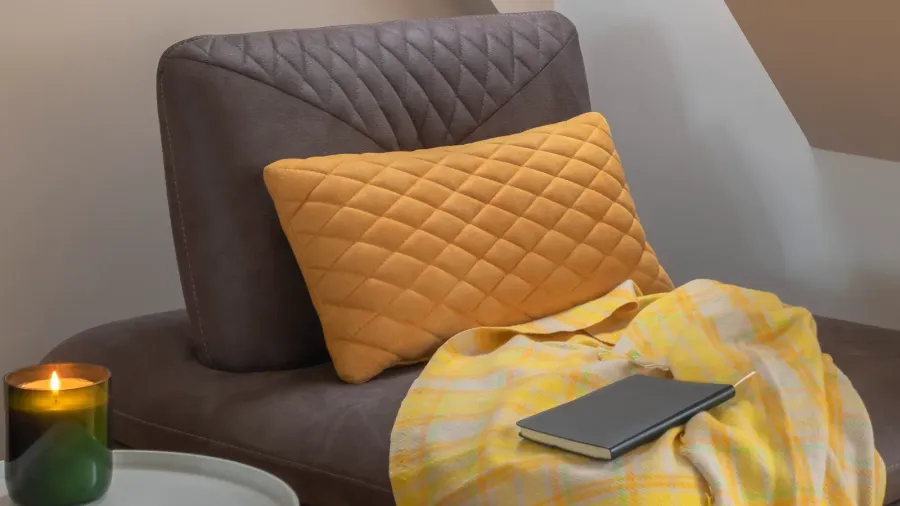 A cozy reading nook by the window with yellow blanket and pillow, and a burning candle.