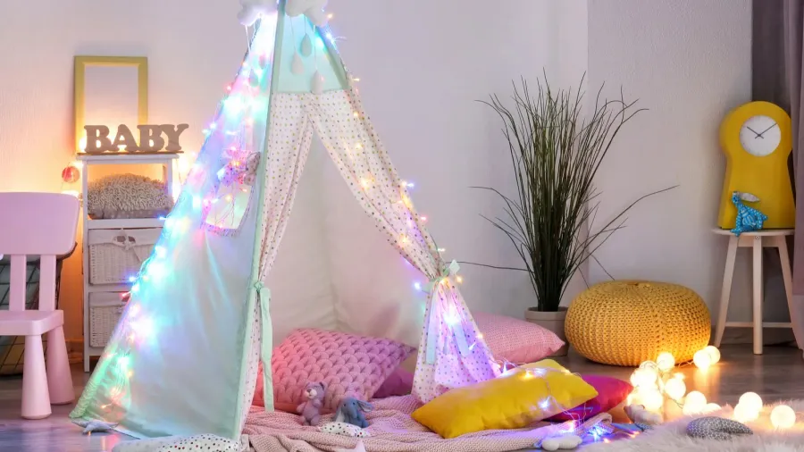 A colorful playroom interior with a canopy tent, colorful throw pillows, stuff toys, rug, and colorful string lights.