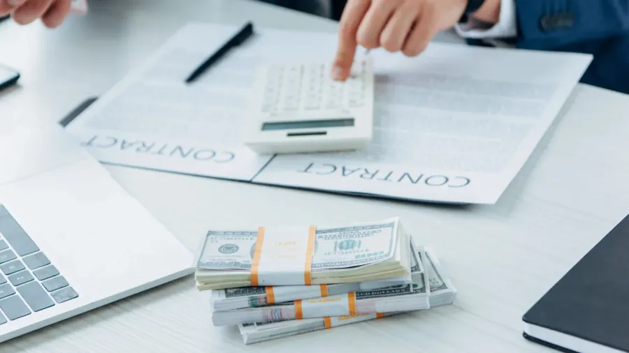 a business setting with a calculator, contracts, and stacks of money.