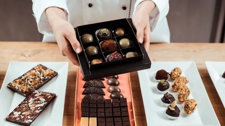cropped view of chocolatier holding box with fresh made chocolate