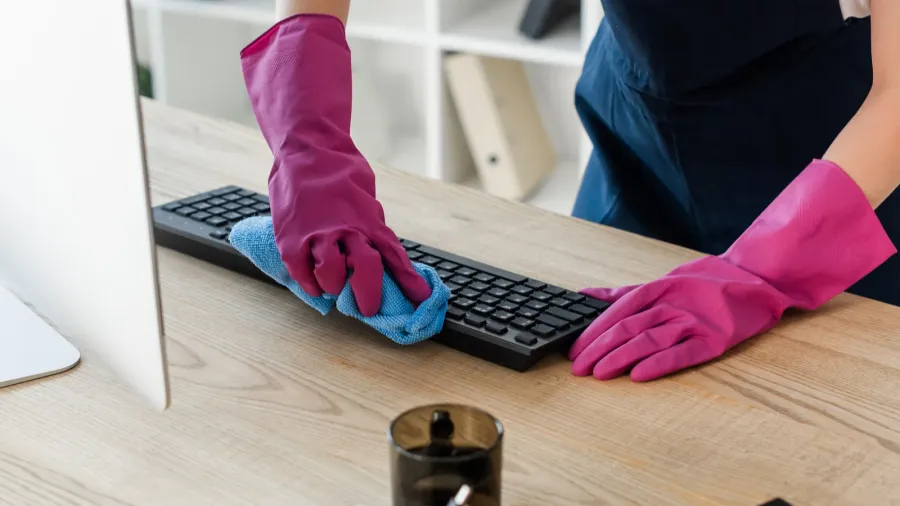 cropped view of cleaner in rubber gloves cleaning computer keyboard