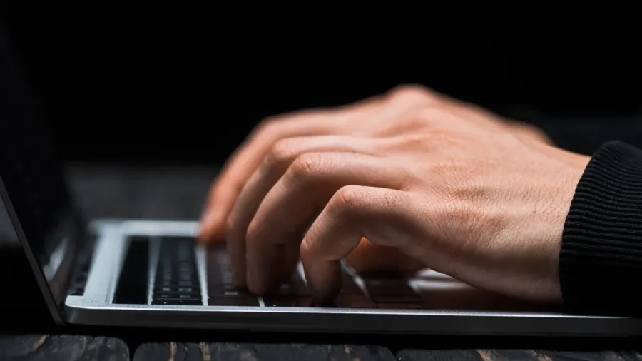 cropped view of hacker typing on laptop keyboard isolated on