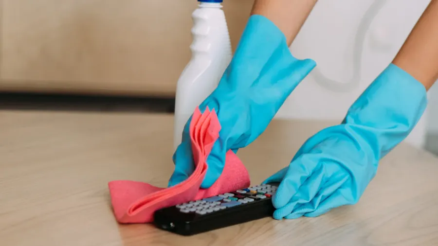 cropped view of woman in rubber gloves cleaning remote controller