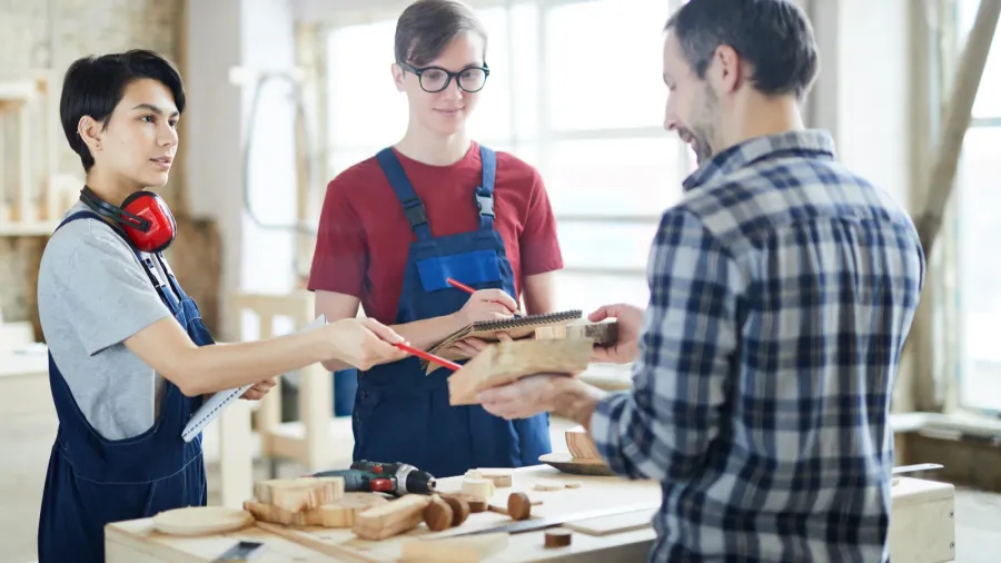 curious young carpenters in overalls standing at desk with wooden