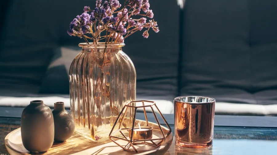 A wooden decorative tray with vases, glass jar with lavender, and candle on the table.