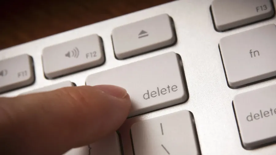 A person holding their finger over the 'delete' key on a white keyboard.