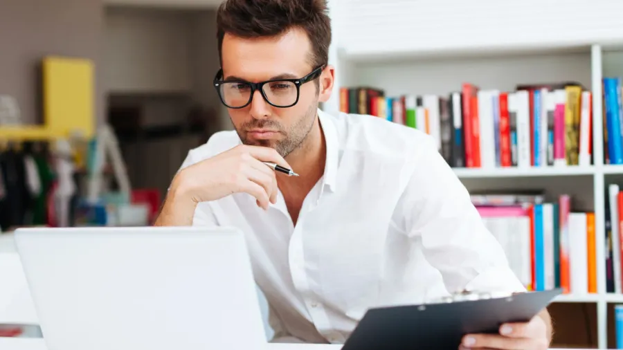 A designer with a pen and board in hand looking at a laptop.