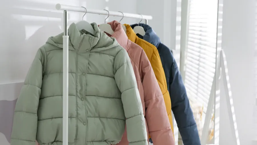 Colorful puffer jackets hanging on a rack in a bright room.