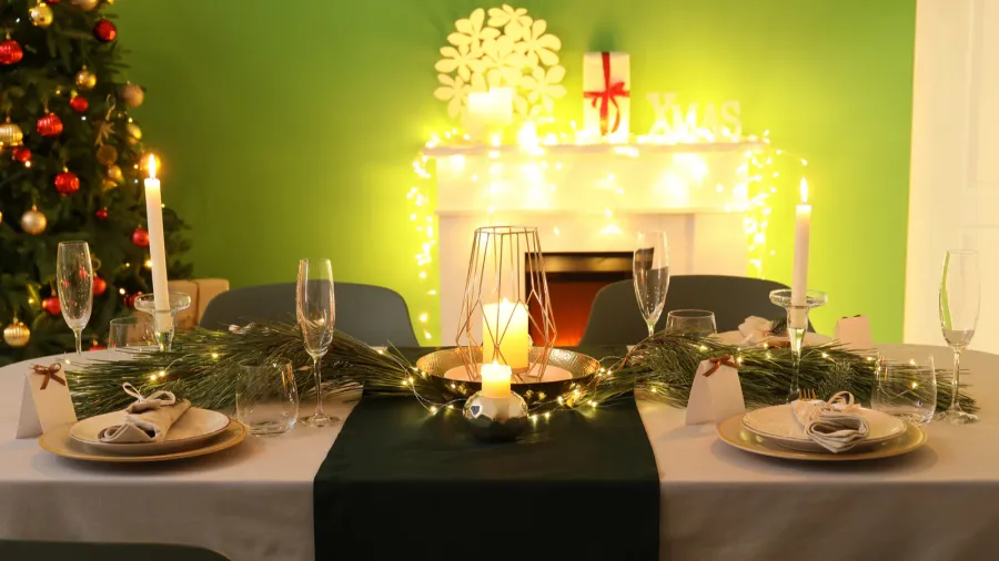 A beautiful dining table setting with dinnerware with napkins, glassware, burning candles, decorative tray, and string lights.