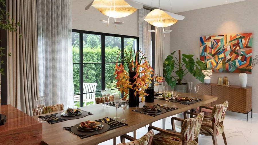 An inviting dining area features a beautifully set table with vibrant floral arrangements, modern artwork, and ample natural light from large windows.