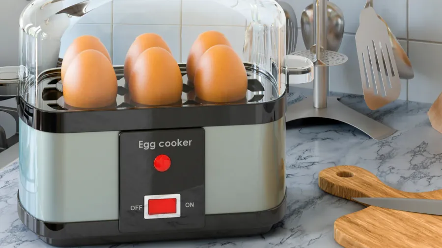 An egg cooker with eggs in it on a marble countertop in a kitchen.