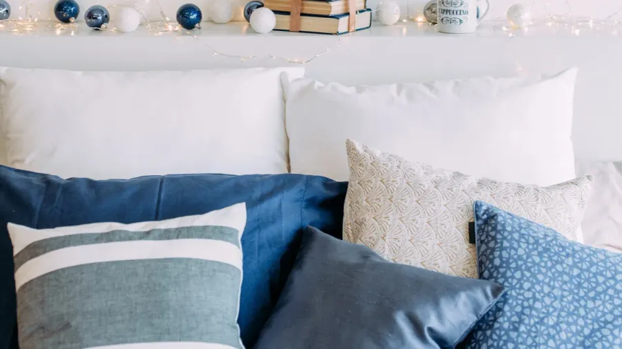 Elegant Christmas interior. White sofa and blue pillows. White and blue baubles, books, and mug in the background.