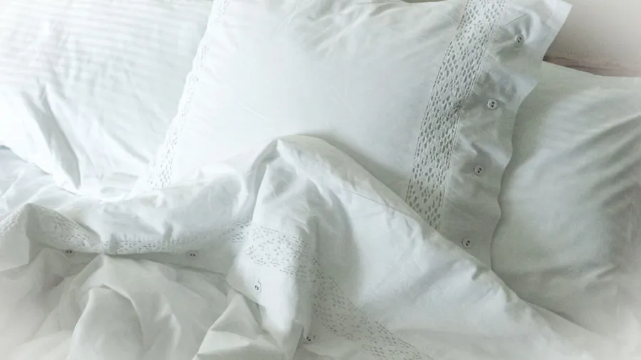 Bed with white embroided sheets and pillowcases.