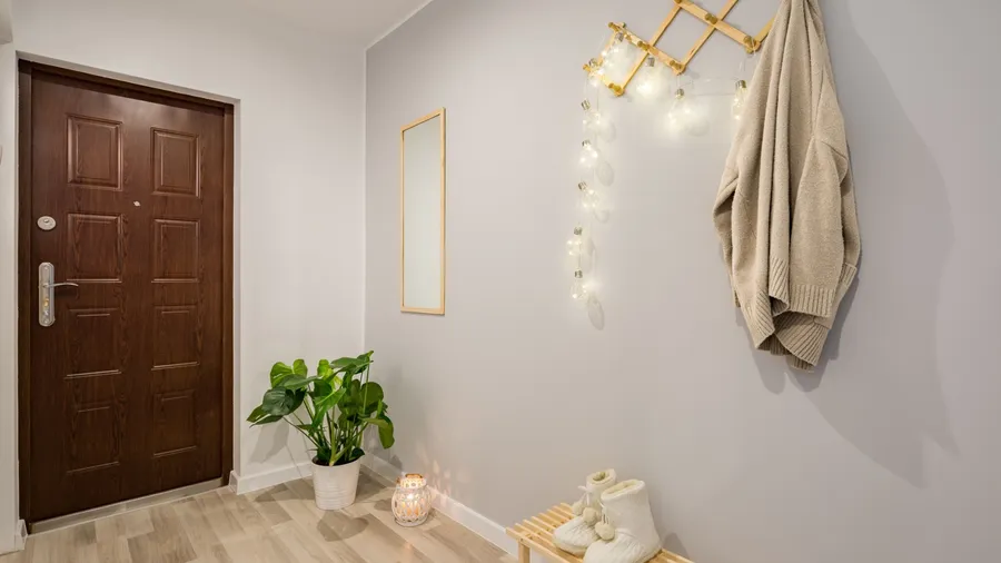 A cozy entryway with a wooden door, potted plant, mirror, coat rack, bench, and lantern
