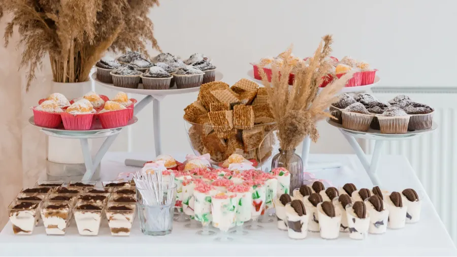 An exquisite dessert table with cupcakes on tiered trays, wafers in a clear glass bowl, mini cheesecakes and pudding in glass cups.
