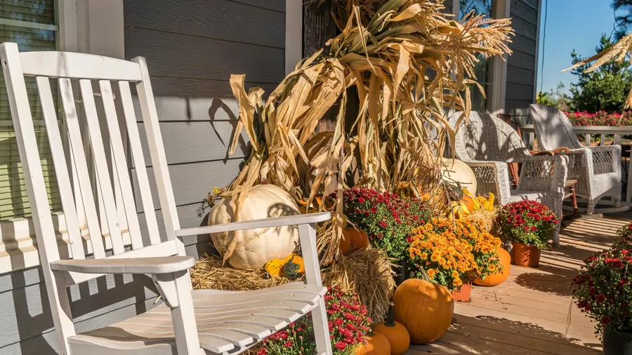 A porch with white rocking chairs, pumpkins, and seasonal flowers.