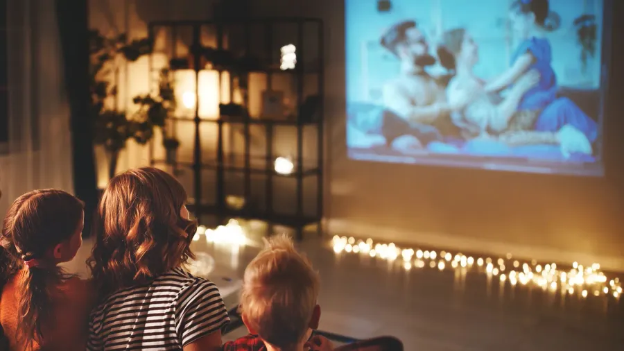 Kids watching a movie together in a cozy, dimly-lit room with fairy lights.
