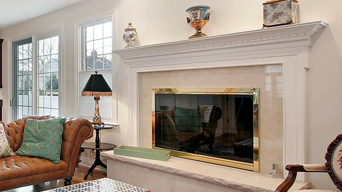 A warm living room with a leather couch, a fireplace with a brass frame, and elegant decorative items on the mantle.