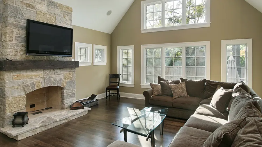 A traditional living room with a stone fireplace, big windows, and neutral-colored furniture.