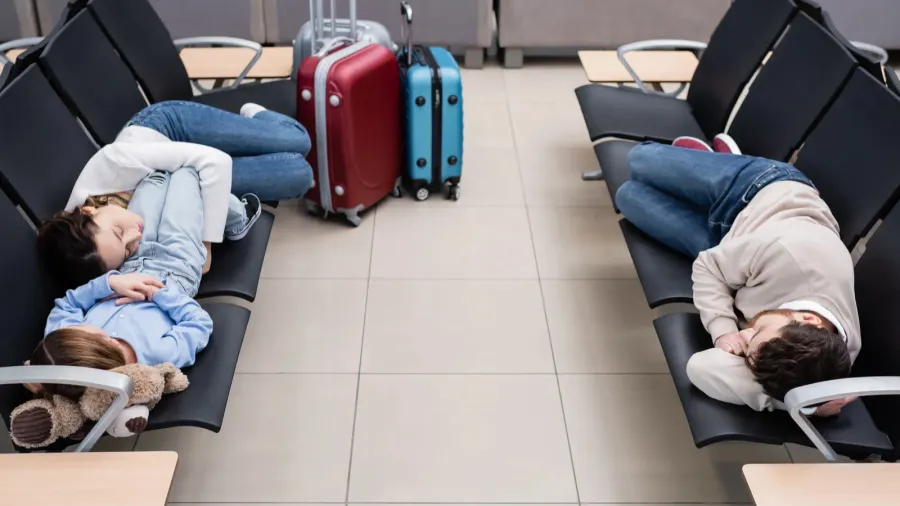 family sleeping on airport seats in departure hall