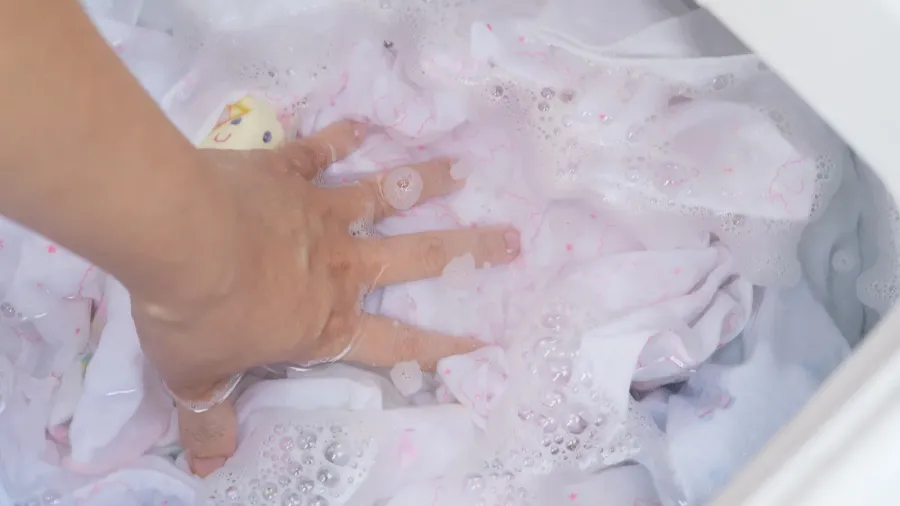female hand touching wet color clothes in water in washing