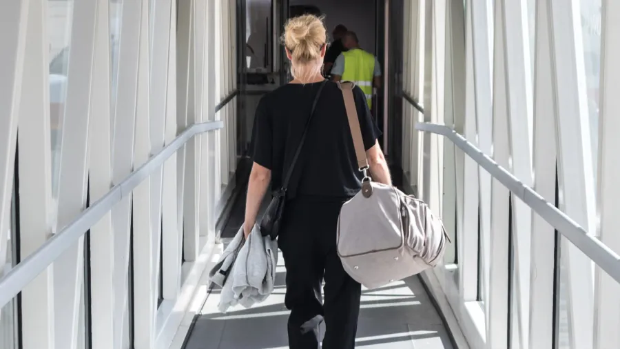 female passenger carrying the hand luggage bag walking the airplane