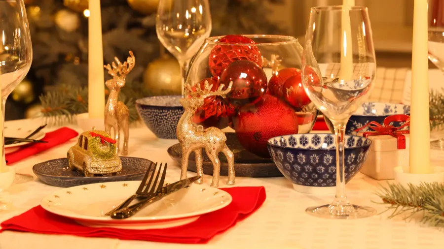 A festive Christmas table setting with red and blue decorations, reindeer figurines, and a glass bowl filled with ornaments.
