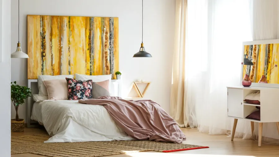 A cozy bedroom with a bed, pillows, artwork, and curtains.