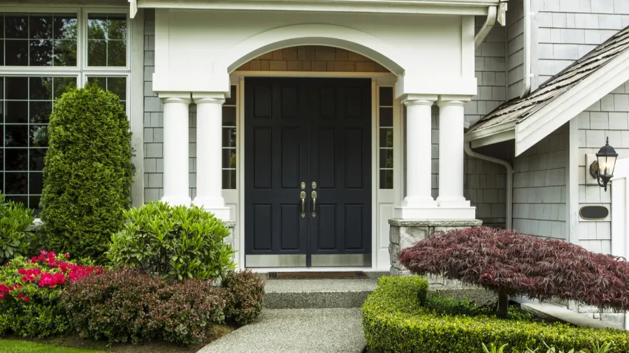 A charming entryway with a dark front door, columns, and well-kept landscaping.