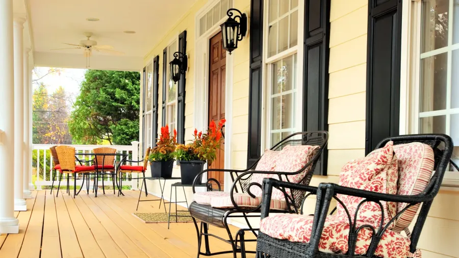 A porch with woven chairs with cushions, a small dining area, and wall sconces.