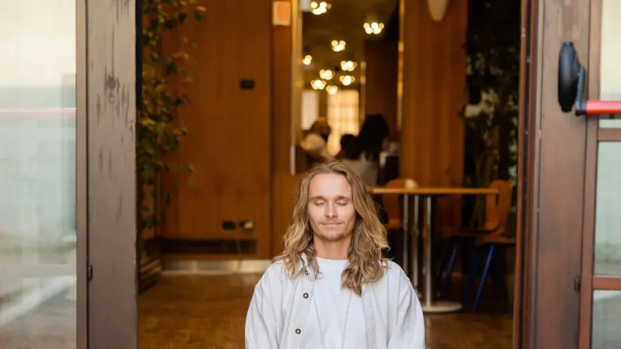 full length of barefoot man in white linen clothes meditating in easy pose near cottage entrance door