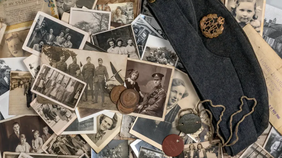 A group of old black-and-white photos, army badges, dog tags, and a dark soldier's hat placed together.